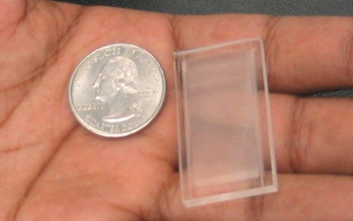 A small transparent microfluidic chip held in a palm next to a quarter